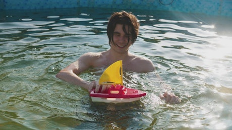 A young man in the pool with a toy boat
