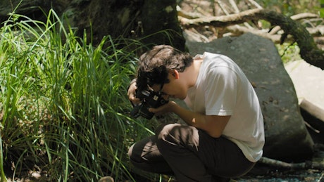 A young man taking natural pictures over a rock in the creek.