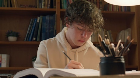 一个穿着连帽衫的年轻人晚上拿着计算器在图书馆学习
