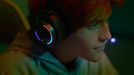 A young man wearing stylish RGB headphones enjoys the gaming session.