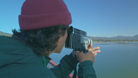 A young man with a retro film camera filming the lake.