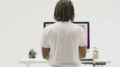 A young man with dreadlocks is working standing on a modern computer.