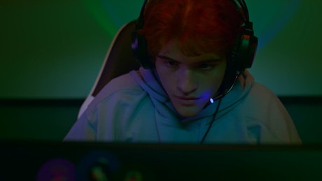 A young man with headphones enjoying the gaming session in front of the computer monitor.