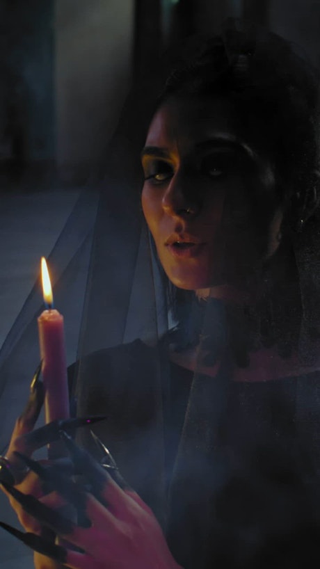 A young mystical woman with blank eyes and a black veil holds a candle while praying.
