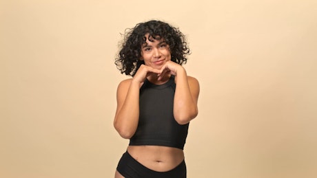 A young natural woman with curly hair shakes her head to the camera over a minimal beige photo studio background.