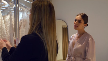 A young sales woman show the details and fabric of bridal dresses to a young customer woman.