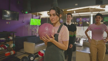A young smiling woman males a bowling shot.