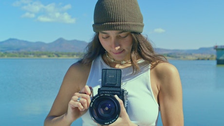 A young smiling woman with a knit hat using an old fashioned camera.