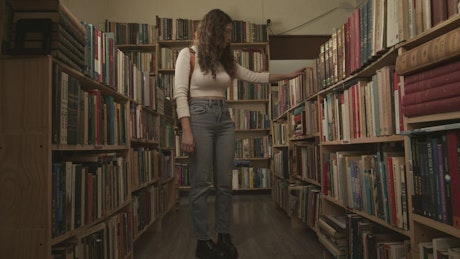 一位年轻的女学生跪下来从图书馆的书架上挑选一本书