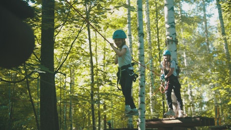 A young woman and her daughter crossing on a rope in the forest.