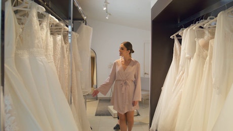 A young woman checking bride dresses with a sales woman assisting behind her.
