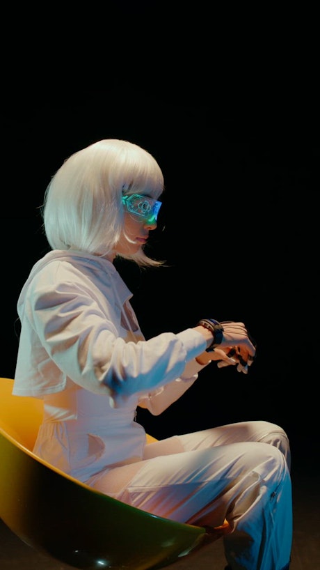 A young woman dressed in a white futuristic suit and a white hair controlls the digital realm with her hand movements and her RGB futuristic VR glasses.