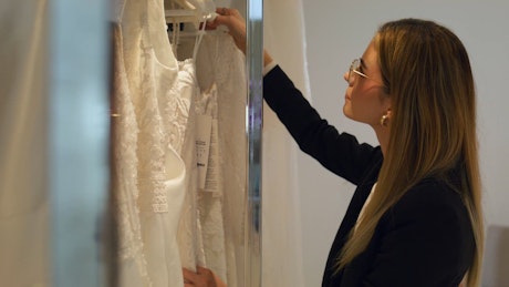 A young woman select a beautiful white bride gown with aeager and smiling customer waiting to try it on.