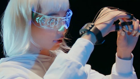 A young woman wearing a futuristic VR headset and a controller device in her hand slowly moves her hands.