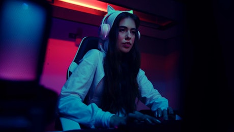 A young woman wearing headphones with RGB lights suddenly gets disappointed in front of the gaming computer.