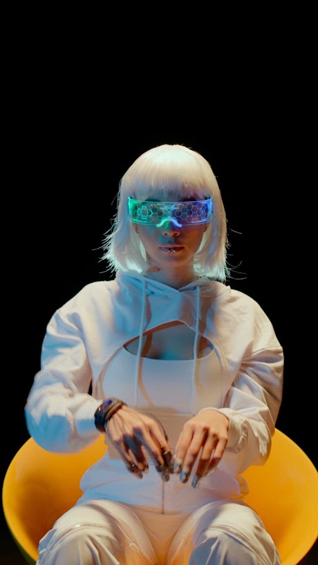 A young woman wearing sci fi VR glasses and a futuristic hand device moves her hands trough the air.