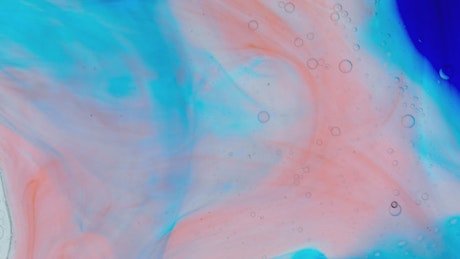 Abstract video of moving pink and blue inks in a liquid.