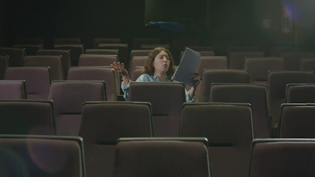 Actress rehearsing a script sitting on the seats of a theater