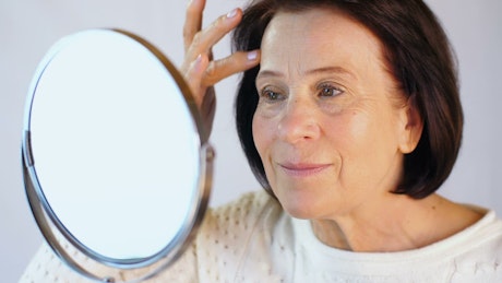 Adult woman looking her face in front of a mirror.