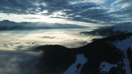 Aerial footage of cloud topped mountains at sunset.