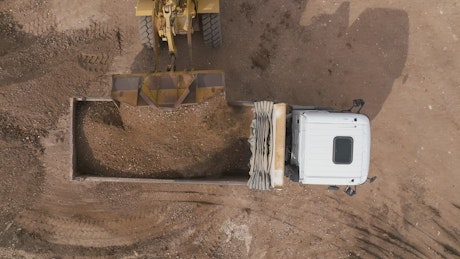 Aerial view of a bucket loader tipping dirt into a loader.