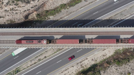 Aerial view of a freight train moving over a busy highway.