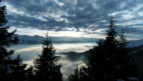 Aerial view of clouds in a valley beneath snowy mountains.
