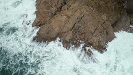 Aerial view of gigantic waves crashing onto rocks.