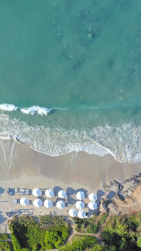 Aerial view of the beautiful turquoise  waves crashing on the sand beach with white umbrellas.