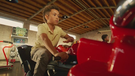 African american little boy on a racing arcade motorbike.