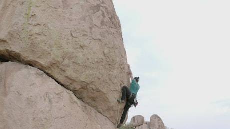 Alpinist climbing a huge rock in a desert