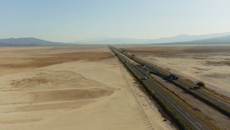 An expansive highway with a steady stream of trucks and vehicles in the middle of the desert.
