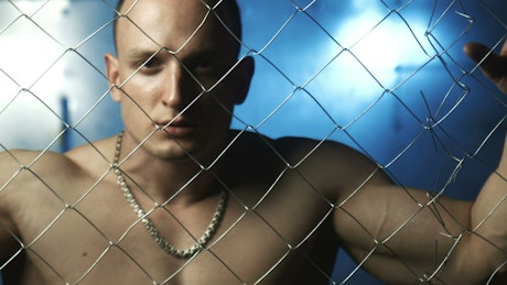 Angry shirtless man behind wire fence
