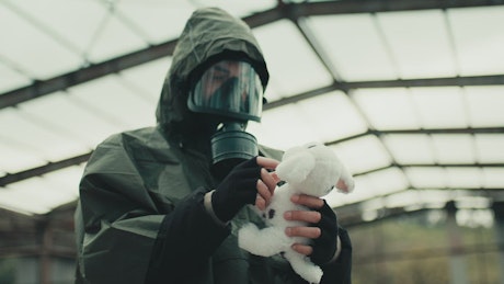 Apocalyptic scene of man in gas mask finding a teddy bear.