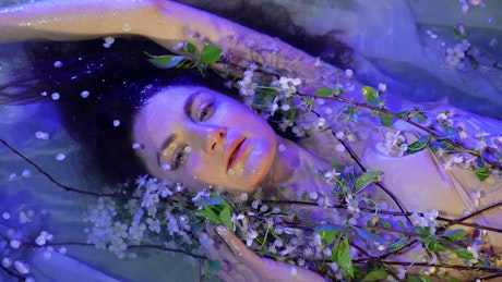 Art concept of a woman covered in flowers floating in the water.