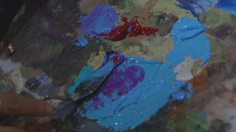 Artist mixing paint on her palette with a spatula.
