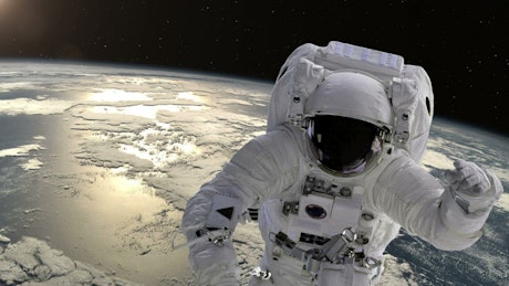 Astronaut in a space suit floating slowly through space above Earth.