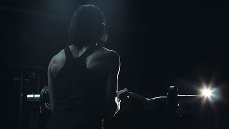 Athlete lifting the barbell in a dark room