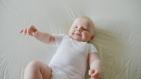 Baby on white bed smiling and reaching