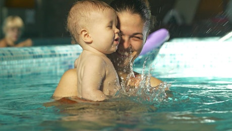 Baby playing in the pool in his mom's arms.