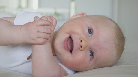 Baby smiles and rolls over in white bedroom