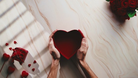 Background of a hand placing a valentine's day heart shaped gift box.