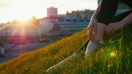 Ballet dancer taking off a slipper sitting on grass.
