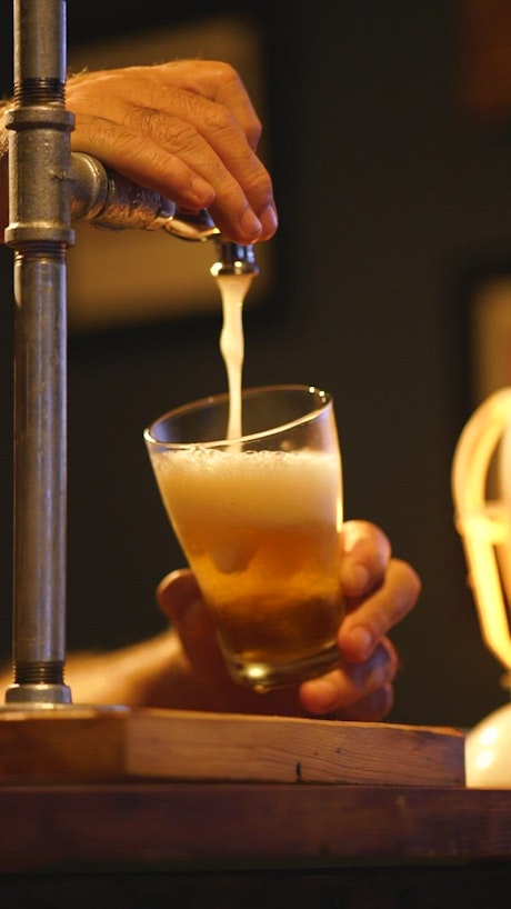 Bartender serving beer from a tap looking down at his hands.