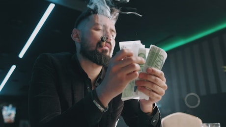 Bearded man counting money while he smokes.