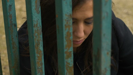 Beautiful woman behind bars looking sadly at camera.