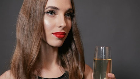 Beautiful woman smiles and sips champagne on dark background.