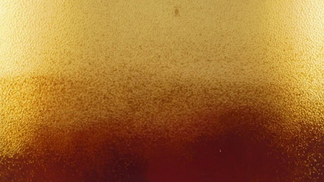 Beer foam forming in a glass seen from close up.
