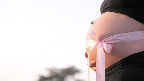 Belly of a pregnant woman with a big pink bow.