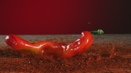 Big red pepper falling into red powder.